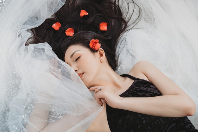 Žena s ružami vo vlasoch, zahalená v bielom závoji leží na posteli.jpg